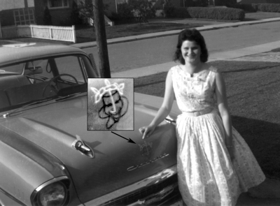 Phil Hennings wife, Betty, with Phil's Chevy
She's pointing to the emblem on the hood (magnified) which was painted by Don Chisolm. This ended up on the drum heads as well as the 1958 championship crest designed by Don.

Photo submitted by Phil Hennings
